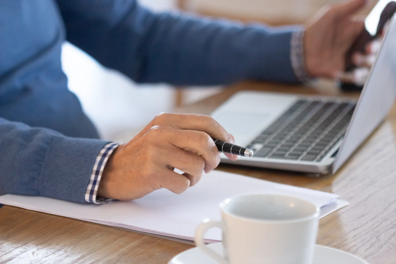 Une main tient un stylo au-dessus d'un document, à côté d'un ordinateur portable