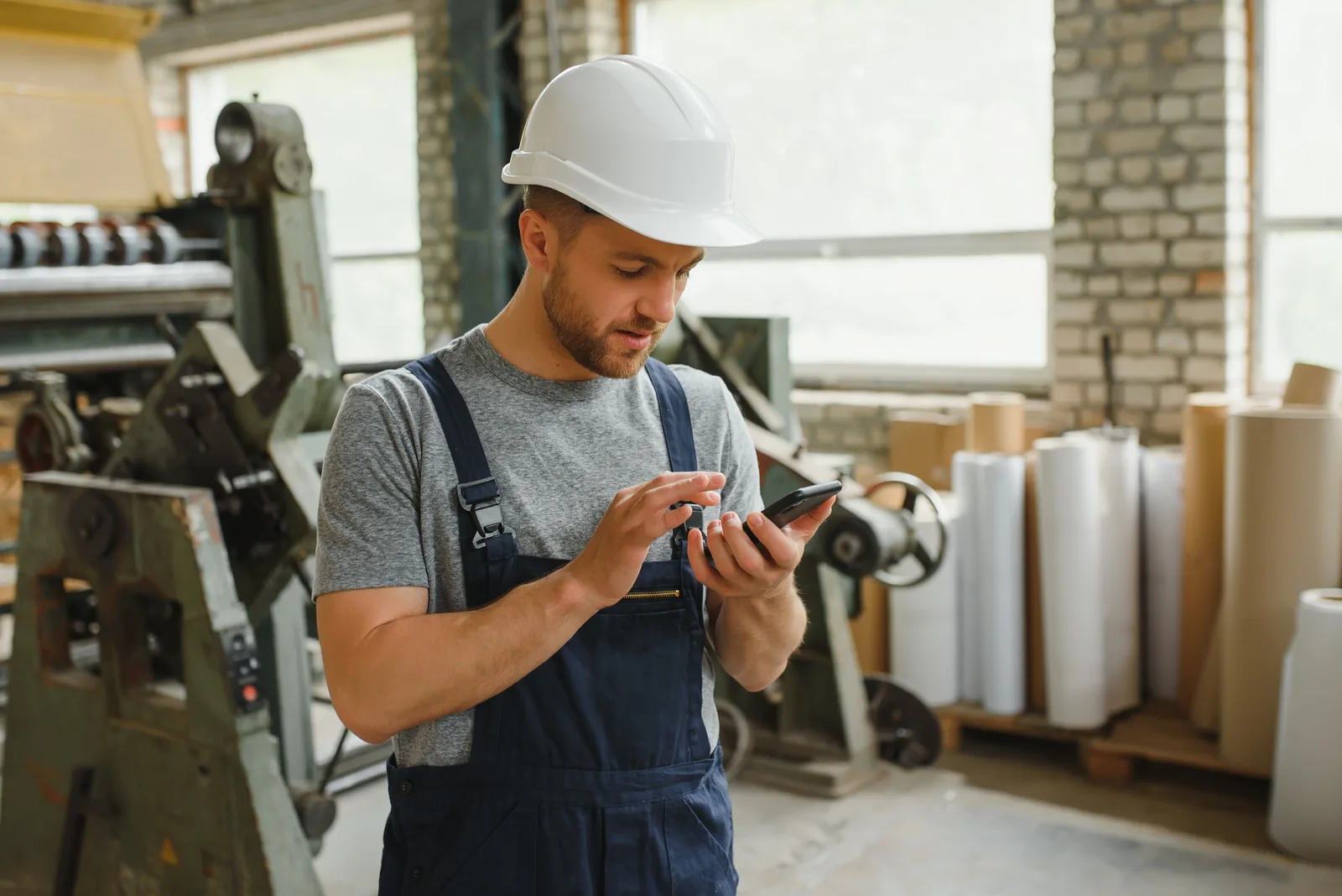 Un ouvrier en salopette consulte son téléphone dans un atelier