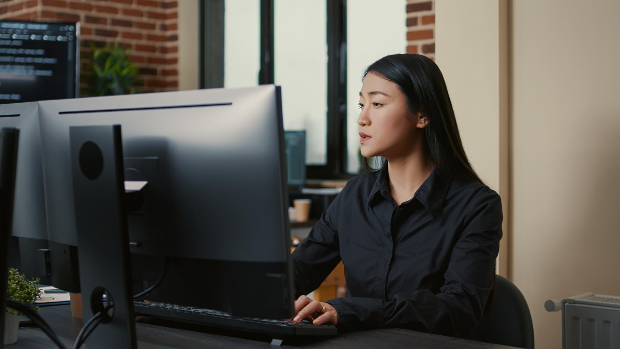 Développeuse au travail dans un bureau d'équipe devant plusieurs écrans