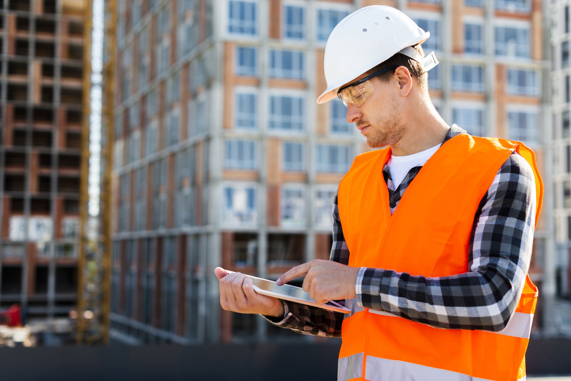 Professionnel du bâtiment préparant un devis sur tablette devant un chantier